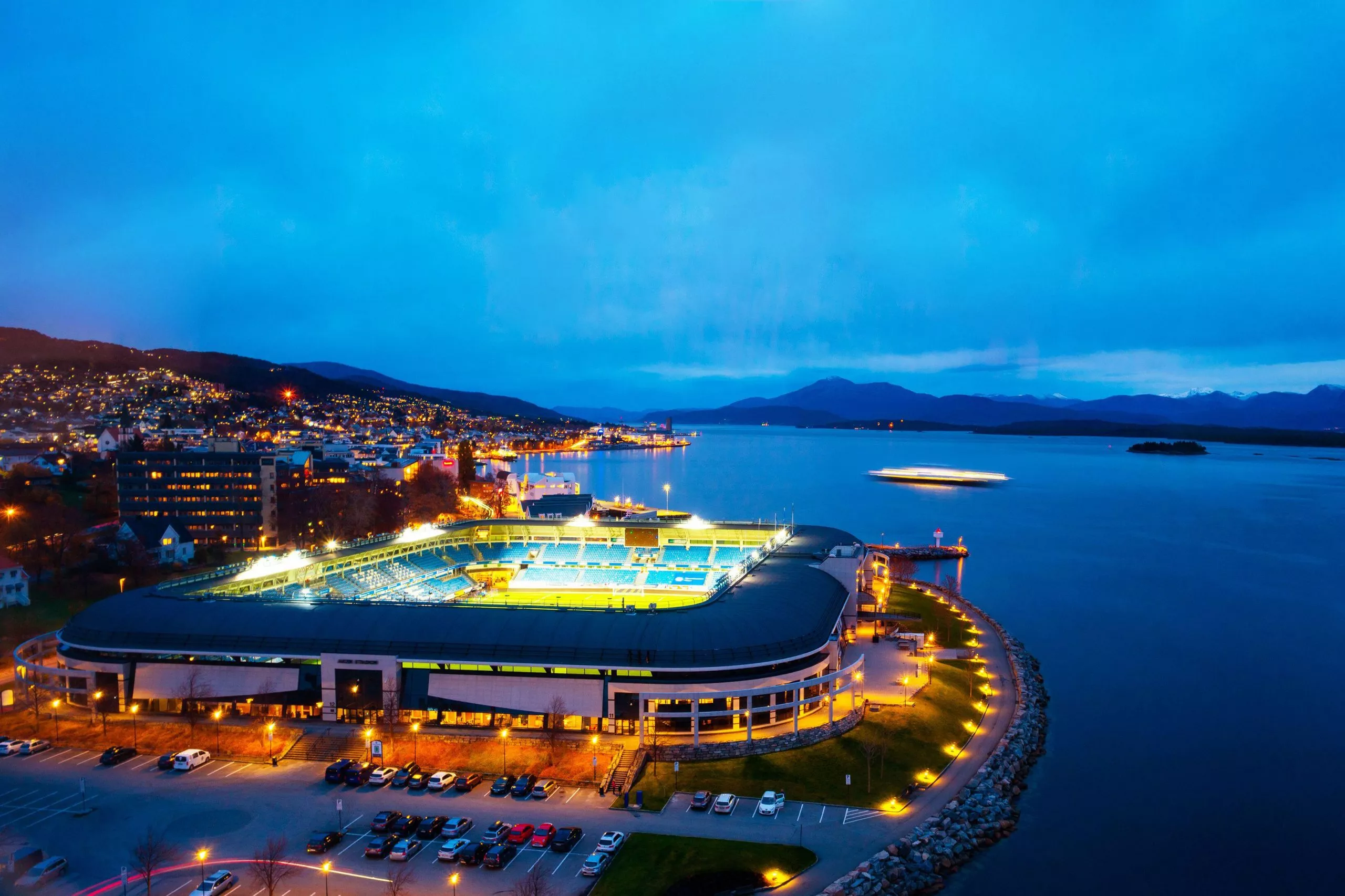 Molde, Norway. Aerial view of town center in Molde, Norway at night. View of the illuminated stadium with sea and mountains at the background